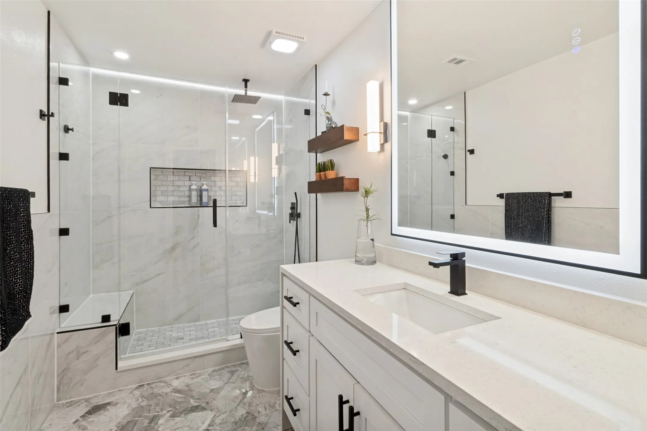 Frameless glass shower enclosure with built-in bench, recessed shower niche, and ceiling-mounted rain shower head