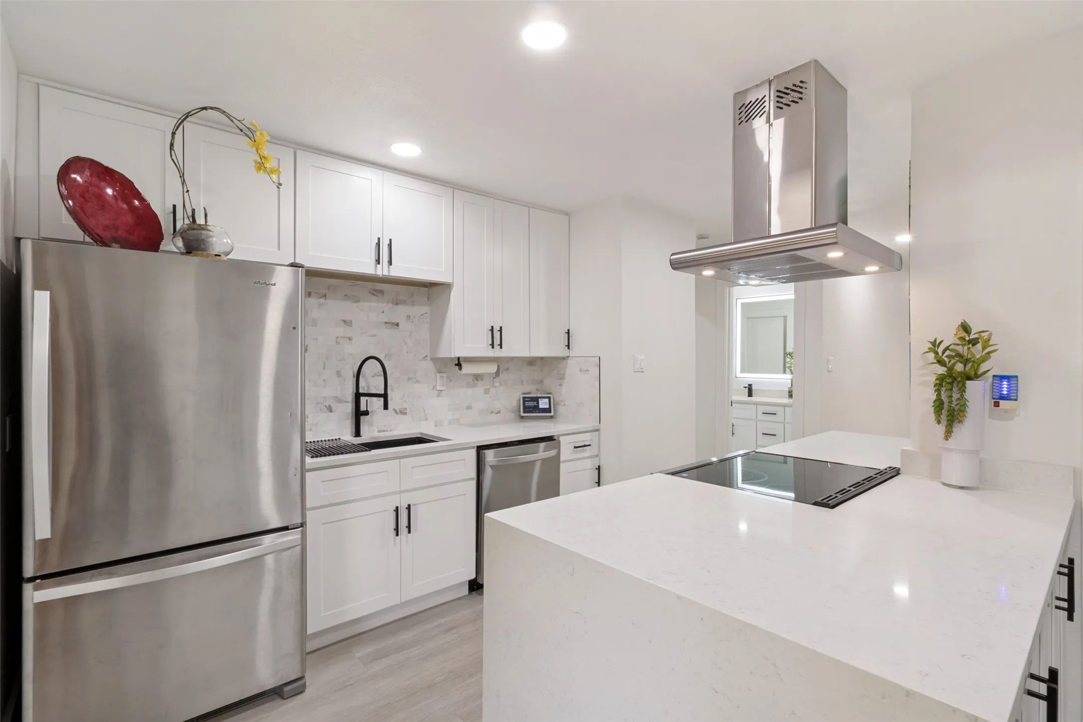 Modern kitchen featuring white shaker cabinetry, stainless steel appliances, a white stone island, and a tile backsplash