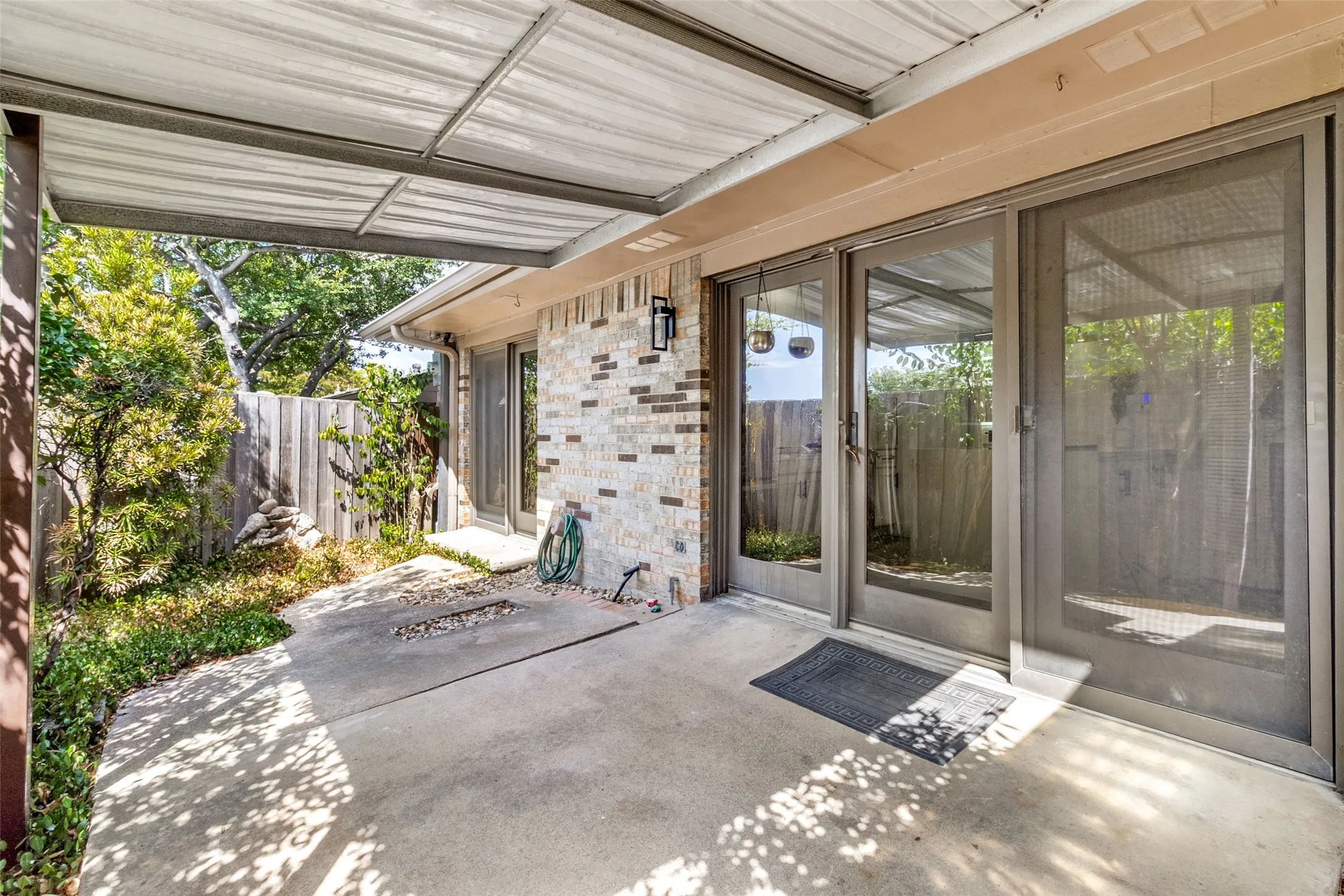 Concrete patio with a corrugated metal awning, brick exterior, and sliding glass doors