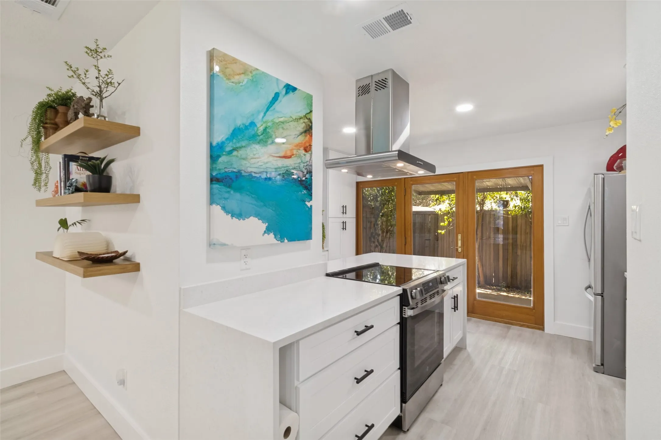 White cabinetry with dark hardware, stainless steel appliances, light wood-finish flooring, and double glass-paneled doors