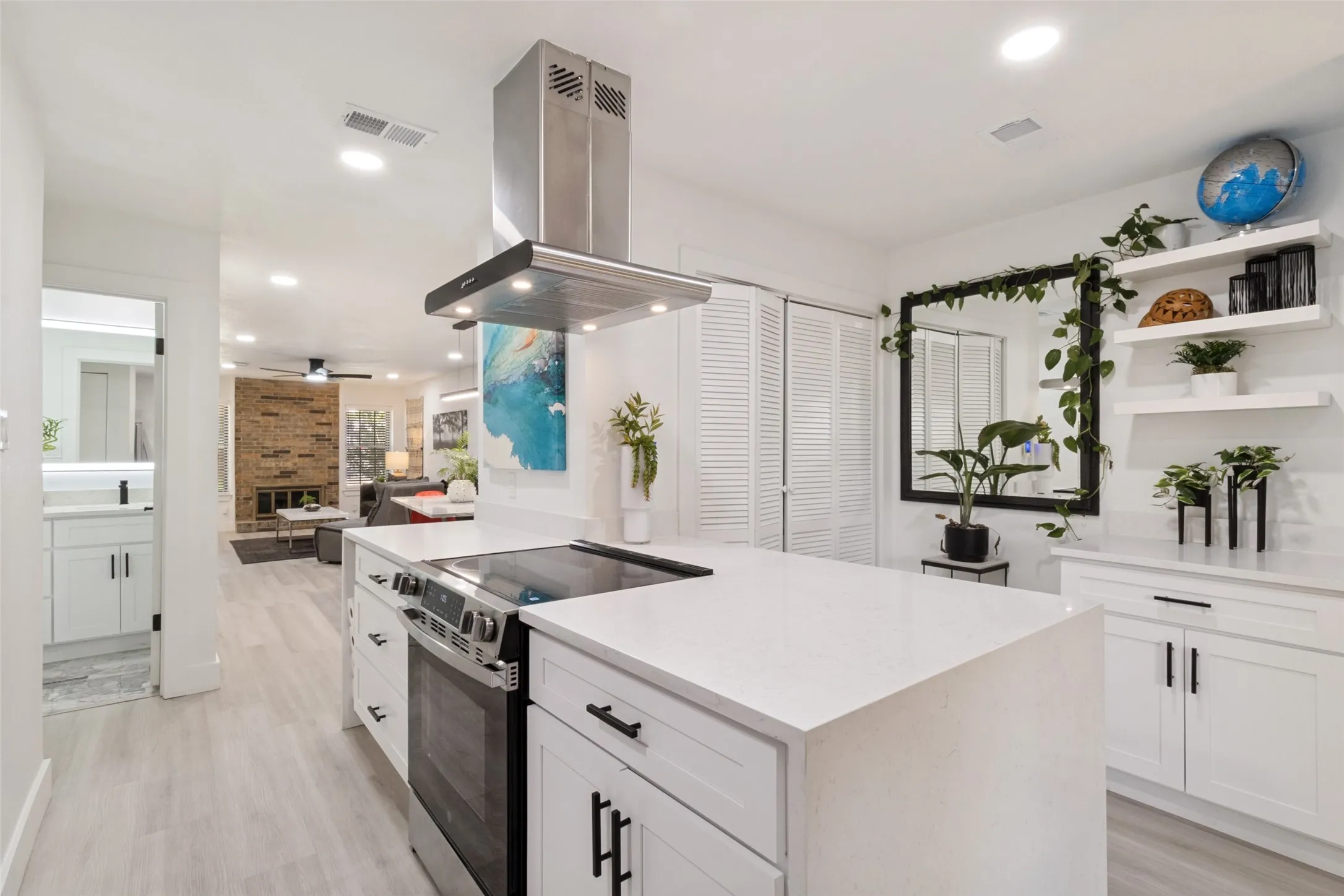 Open-concept kitchen featuring an island with an integrated cooktop, stainless steel range hood, white cabinetry with dark hardware, and wood-finish flooring