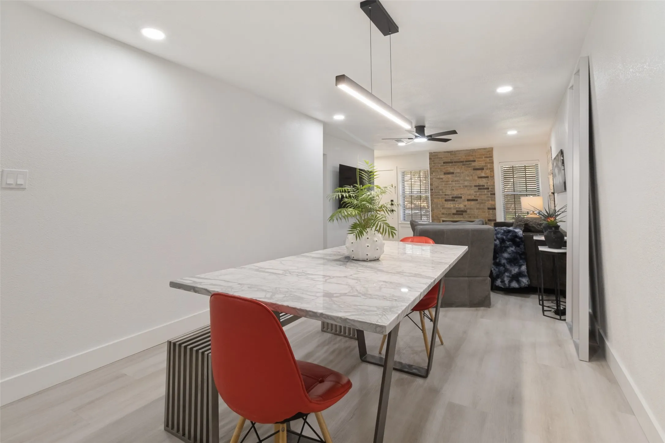 Open-concept living area with light wood-finish flooring, recessed lighting, and a modern linear pendant light fixture
