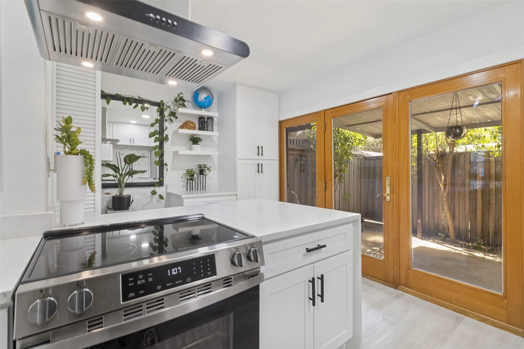Modern kitchen featuring a stainless steel range and hood, white cabinetry, open shelving, and a white countertop