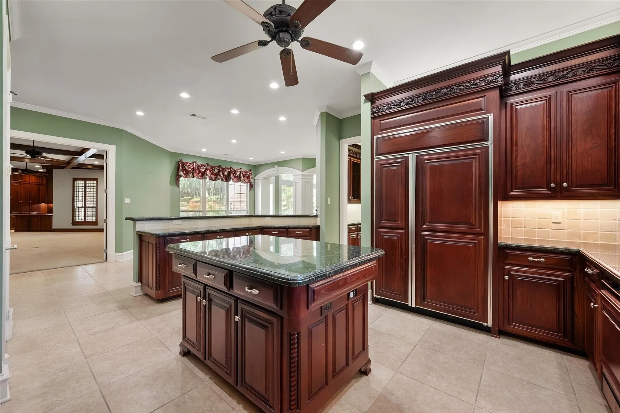 Kitchen featuring rich wood cabinetry with custom trim, a center island with a distinctive stone countertop, built-in panel-front refrigerator, recessed lighting, and tiled flooring