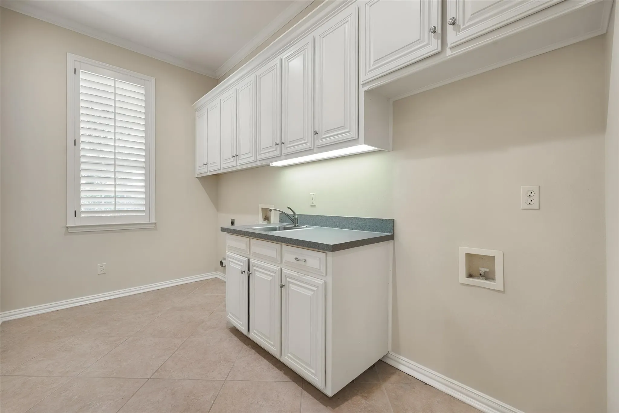 Spacious utility room featuring storage with a large safe for storing valuables with extensive white cabinetry, an integrated sink with countertop, under-cabinet lighting, and tile flooring