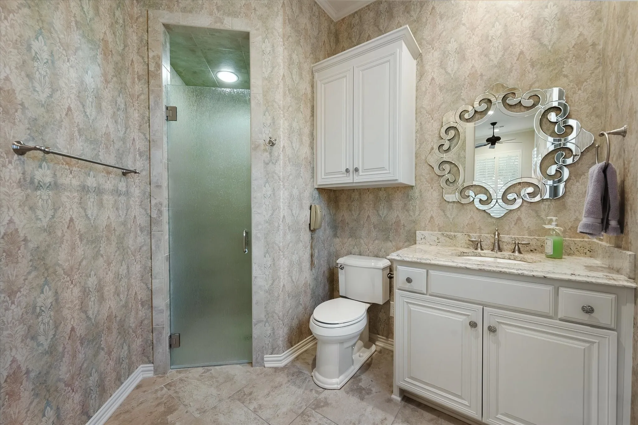 Convenient to the yard and the exercise area, a stone countertop, decorative mirror, and built-in white cabinetry allow for extra shower space