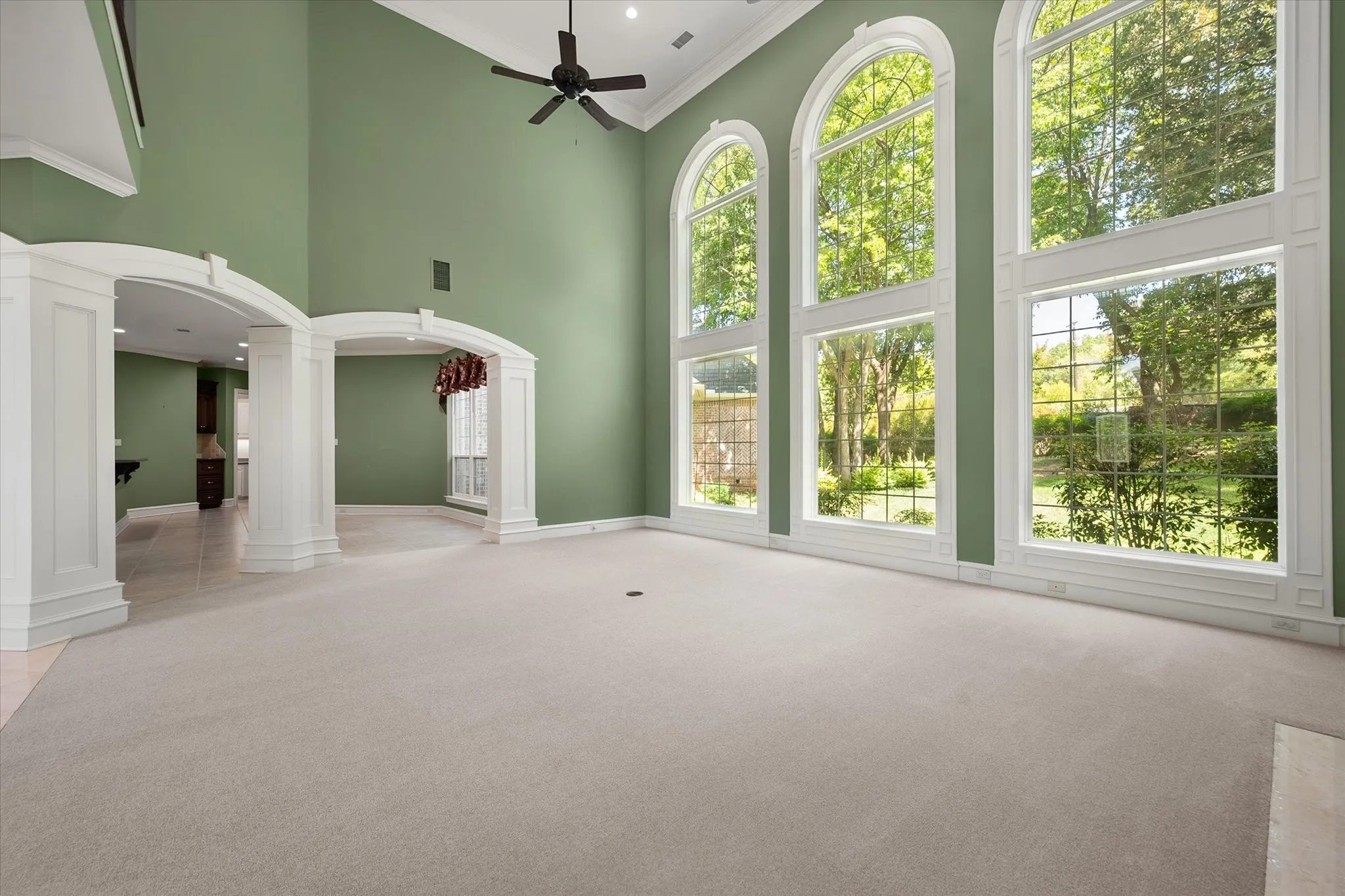 Open floor plan with three distinctive, arched windows, two arched entryways with decorative columns, and plush carpet flooring