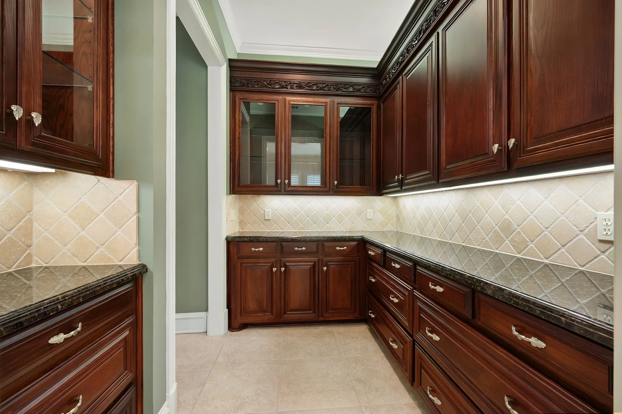 Butler's Pantry adds extra serving and storage areas with rich wood-finish cabinetry, additional outlets, under cabinet lighting  with glass-front accents