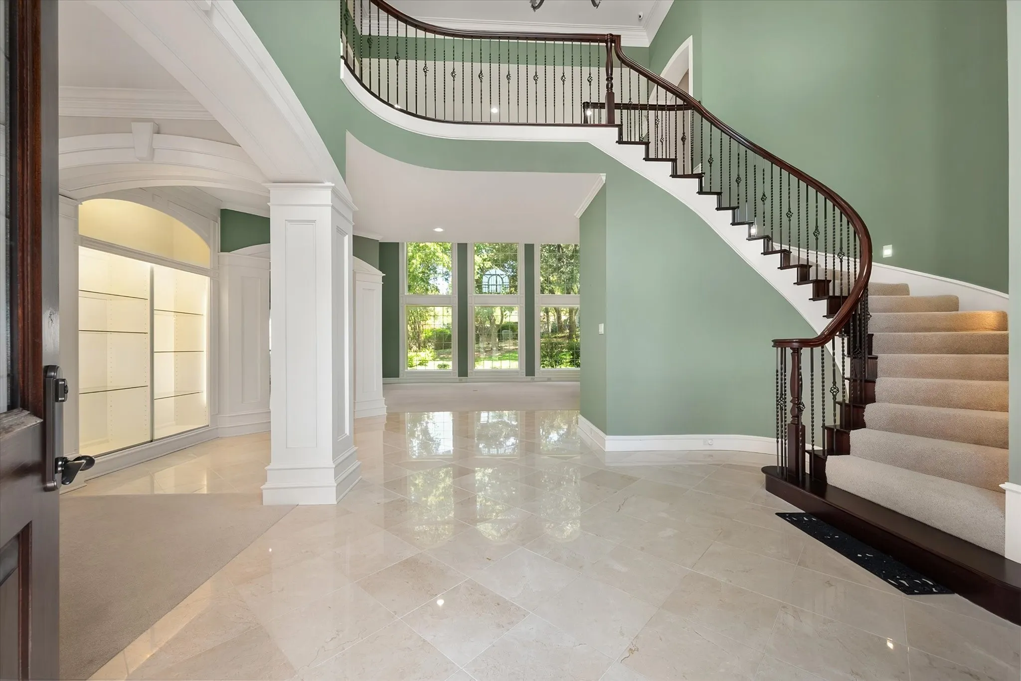 Grand foyer featuring a curved staircase with dark wood banister and wrought iron spindles, large format tile flooring, and tall windows