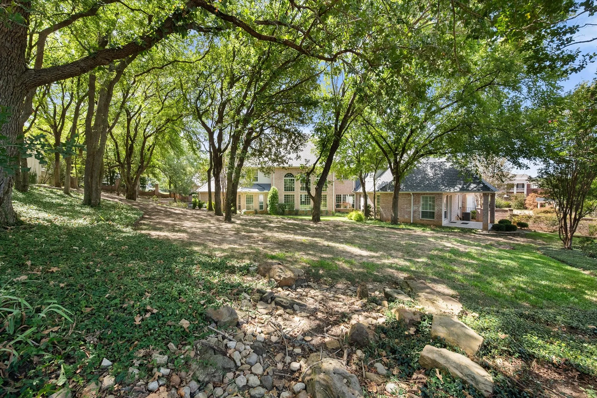 Expansive property with mature trees, a gently sloped lawn, and integrated natural rock features