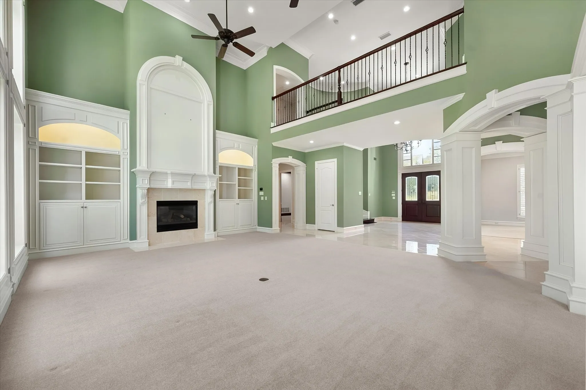 Soaring ceilings with a decorative ceiling fan, a fireplace with integrated built-in shelving, an interior balcony with decorative railing, and arched door frames