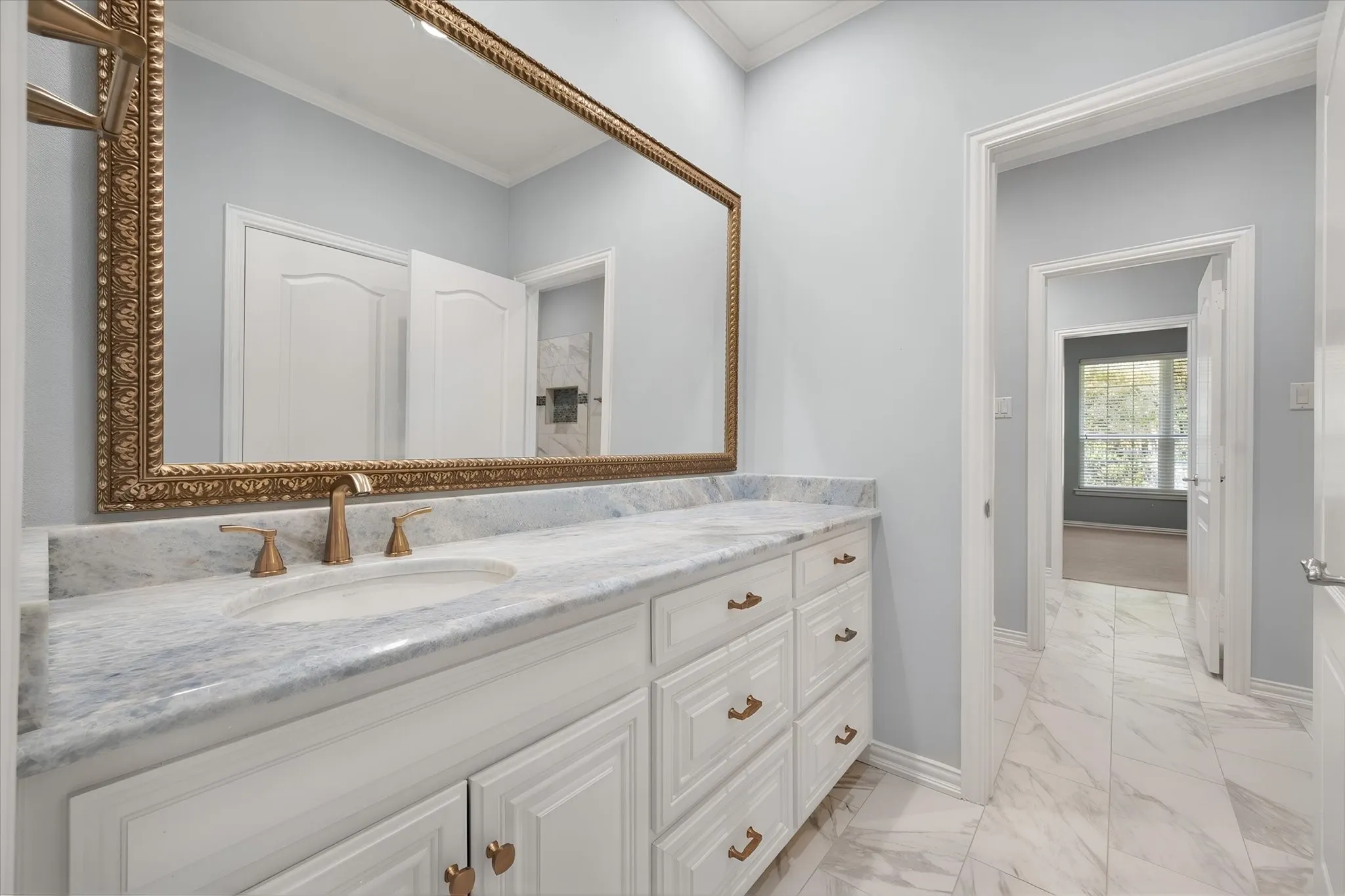 Ensuite white vanity with private sink, storage and walk-in closet with marble countertop, and a large ornate framed mirror