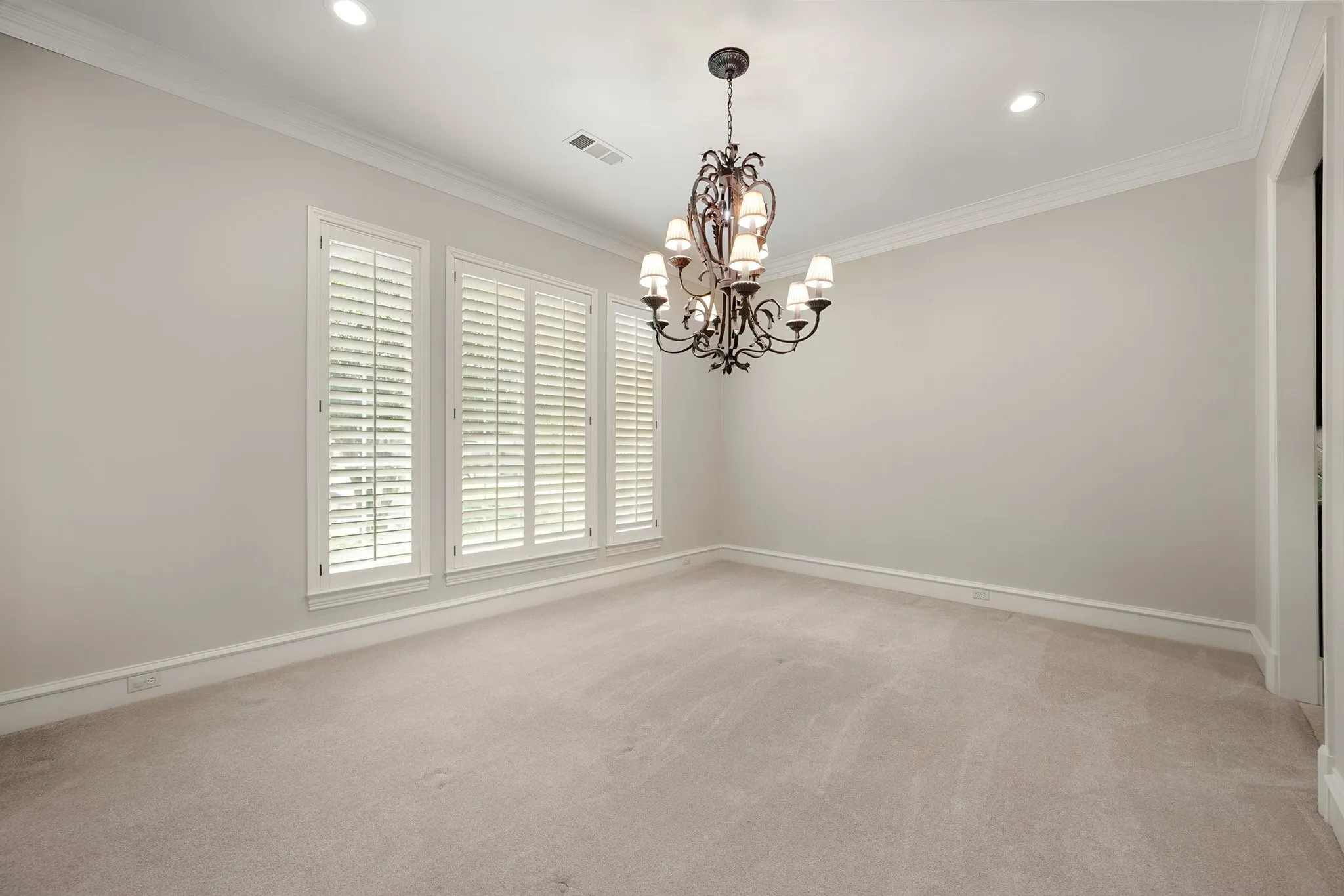 Large dining room with fresh paint, recessed lighting, crown molding, and an ornate wrought iron chandelier illuminate the space