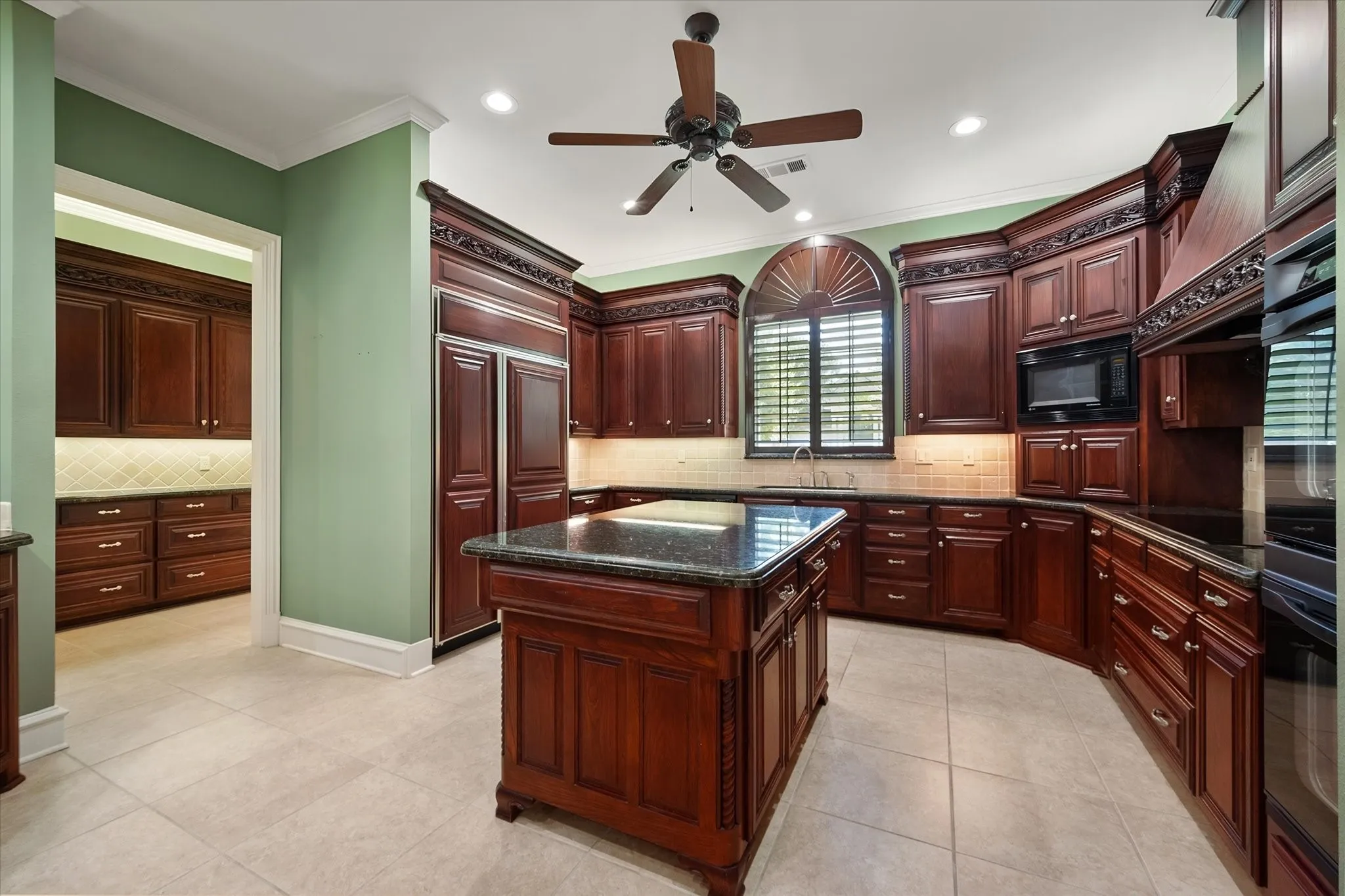 Kitchen featuring custom wood cabinetry, a central island a built-in microwave, and decorative arched windows