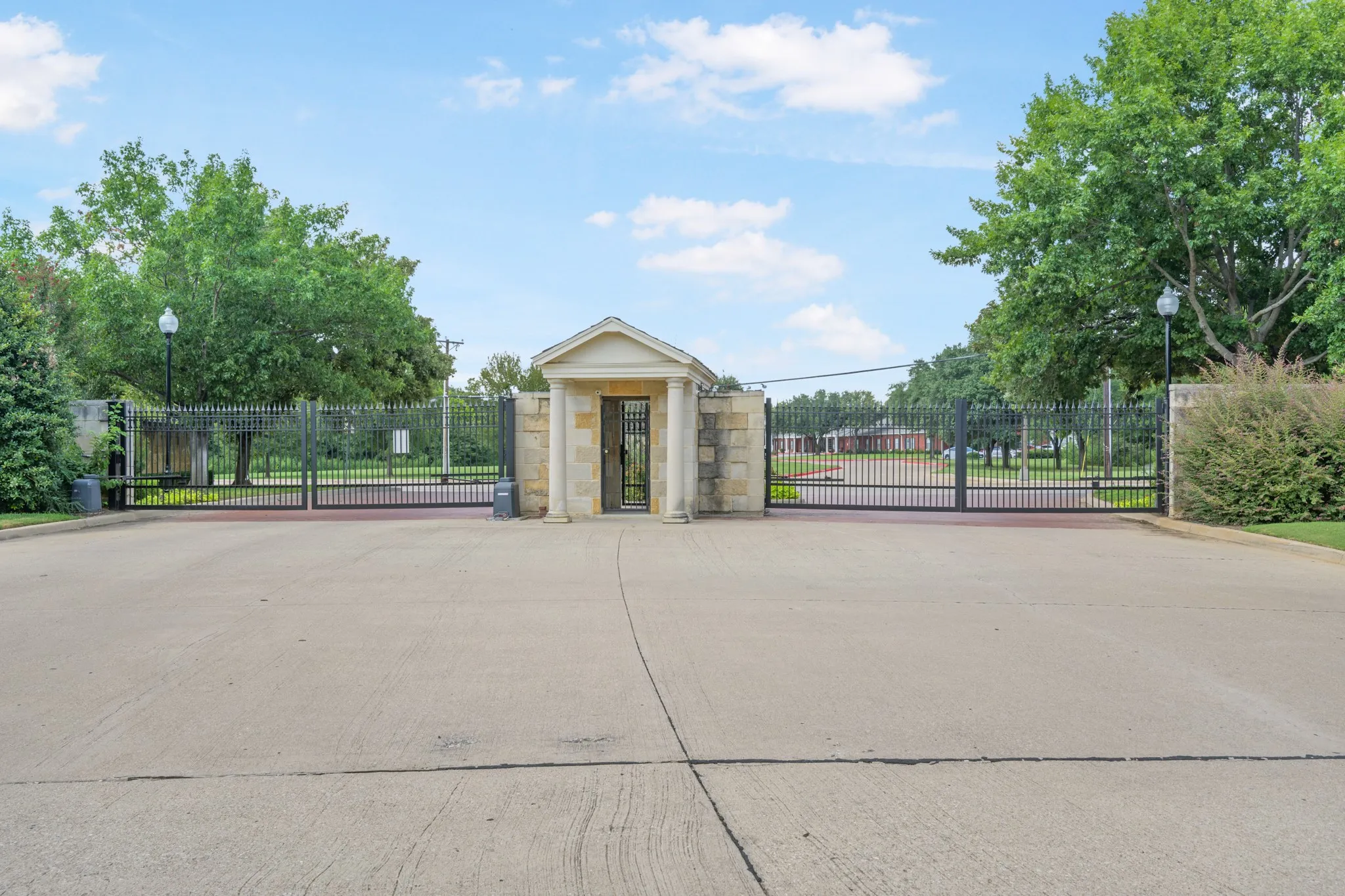Gated entry featuring stone columns, black wrought iron fencing, a pedestrian gate, and mature landscaping