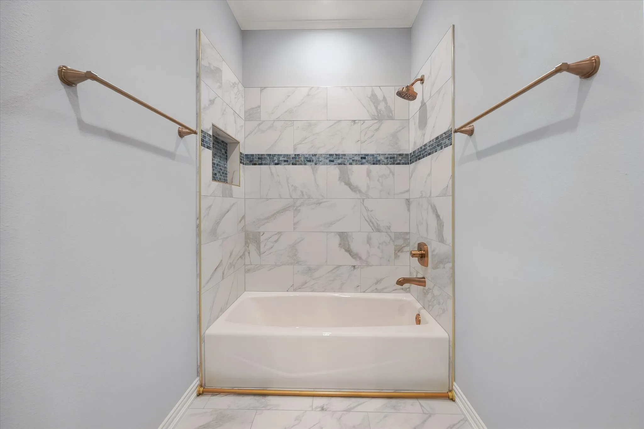 Bathtub and shower combination featuring a tiled surround, recessed shower niche, and brushed gold-tone fixtures