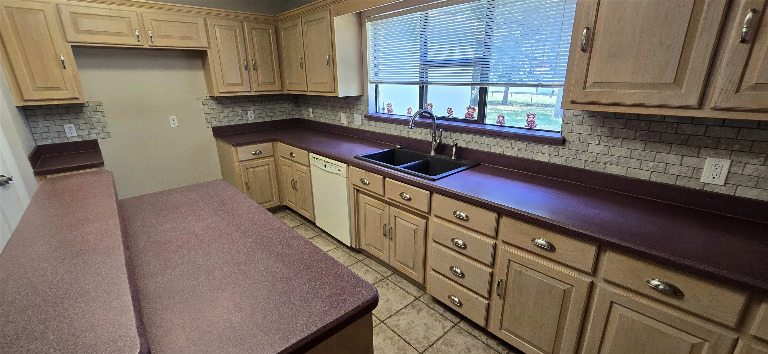 Kitchen featuring extensive wood-finish cabinetry, dark countertops, tiled backsplash, dual basin sink, and a built-in dishwasher