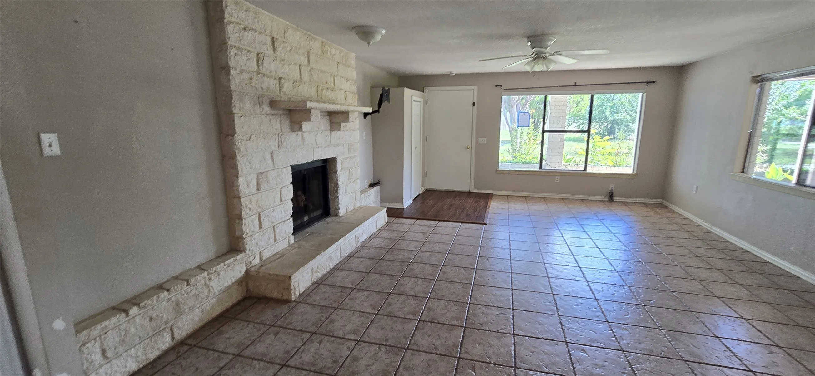 Spacious living area featuring a stone-clad fireplace with mantel, ceiling fan, large windows, and tile flooring