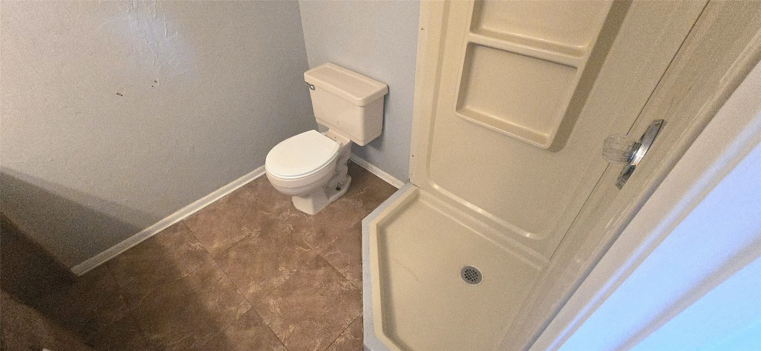 Shower stall with integrated shelving, tile-style flooring, and a toilet