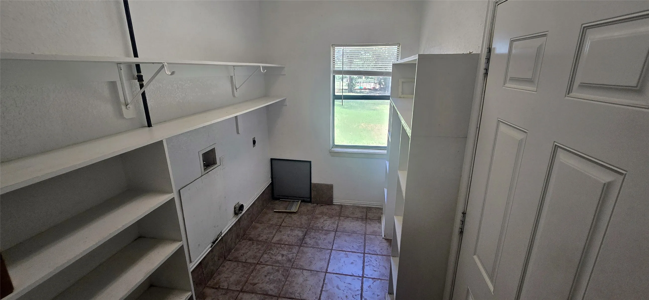 Laundry area featuring white built-in shelving, tiled flooring, and a single window