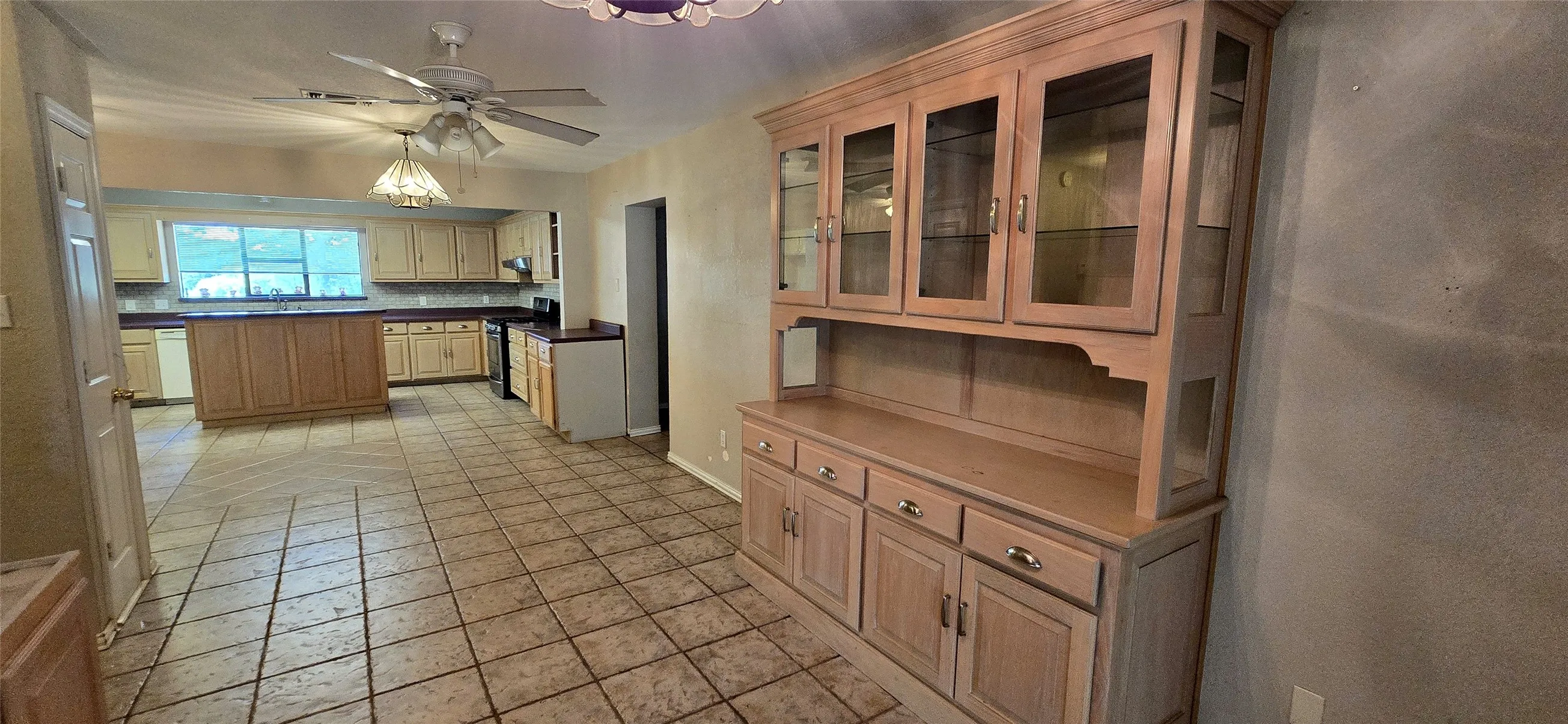 Tile flooring throughout, kitchen island with wood-finish cabinetry, built-in display hutch, ceiling fan with attached light fixture, and recessed lighting