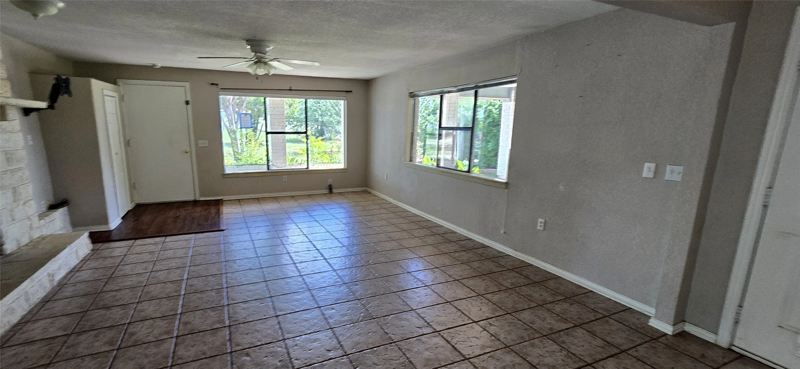 Spacious room featuring large format tile flooring, multiple windows, a ceiling fan, and a painted brick fireplace