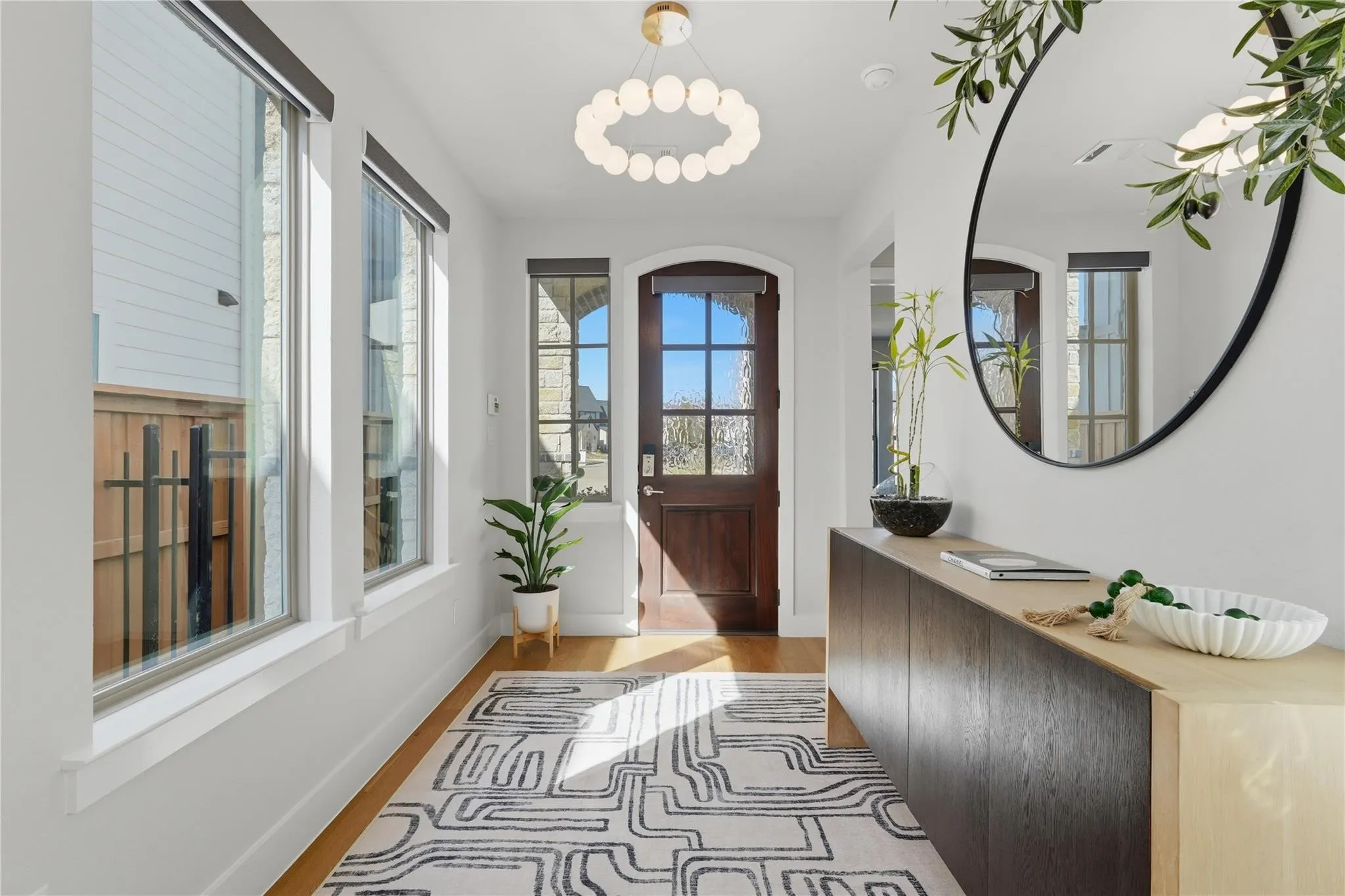 Hardwood flooring, custom wood entry door, modern spherical chandelier, white framed windows, and a built-in console cabinet