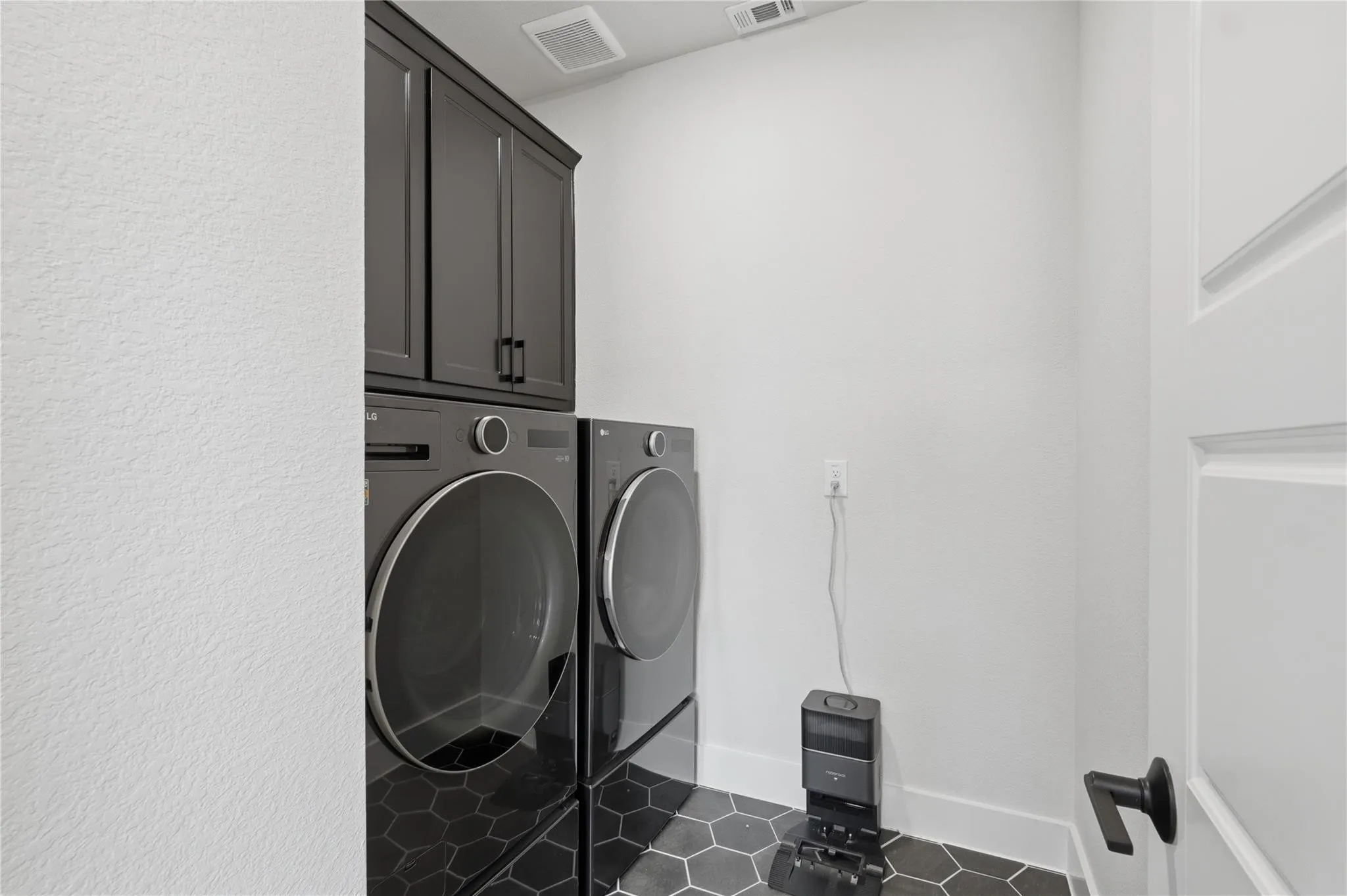 Hexagonal floor tiling, upper cabinetry with dark finish, and a paneled interior door with matte black hardware