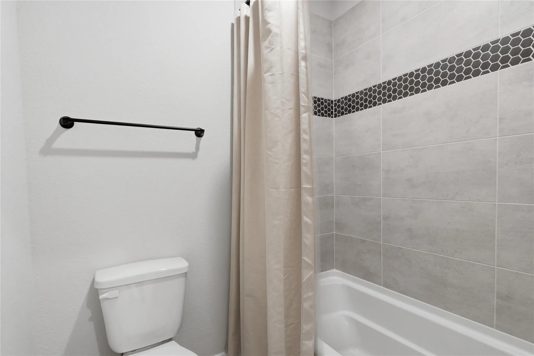 White bathtub with light gray tile surround and black hexagon tile accent band