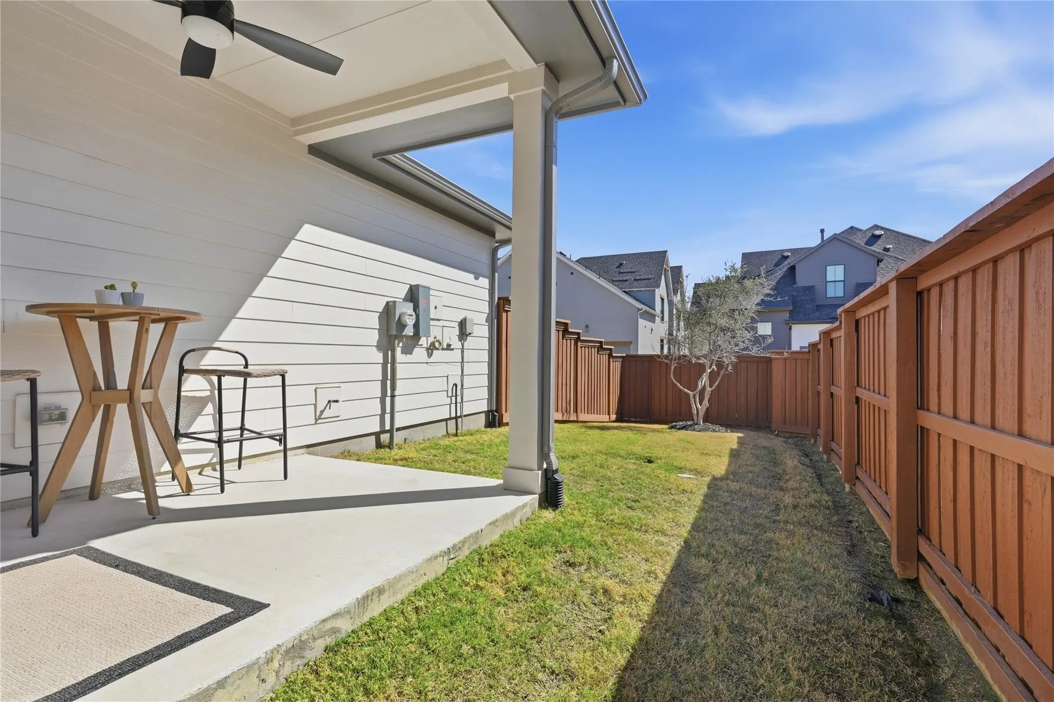 Covered patio with a ceiling fan, white siding, and a fenced yard with grass