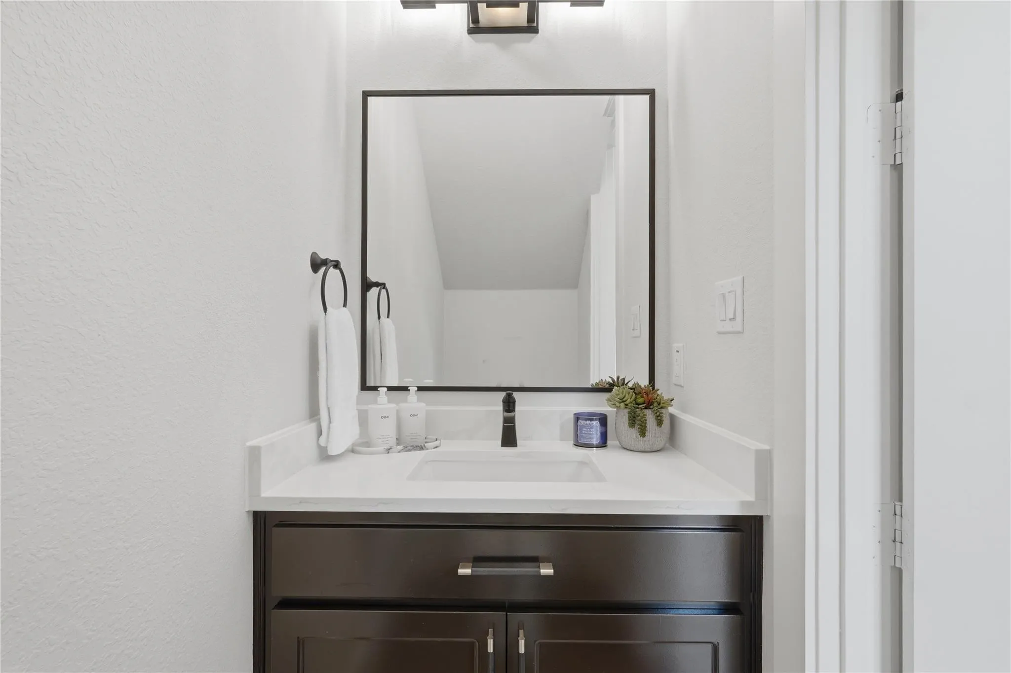 Dark wood-finish vanity with drawer and cabinet storage, under-mount sink, white countertop, and framed mirror