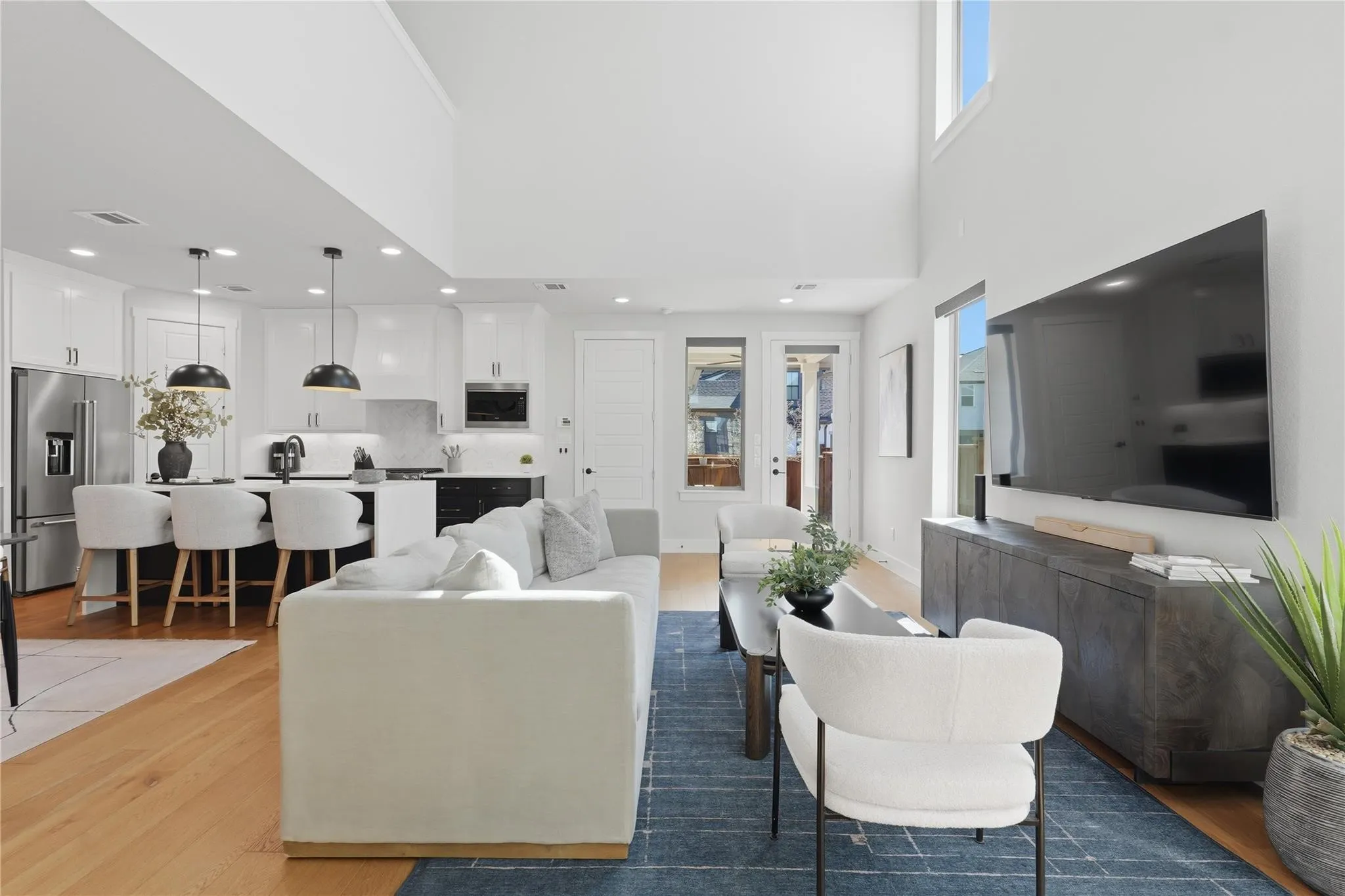 Open-concept living space featuring high ceilings, wood-finish flooring, a kitchen island with seating, stainless steel appliances, and large windows