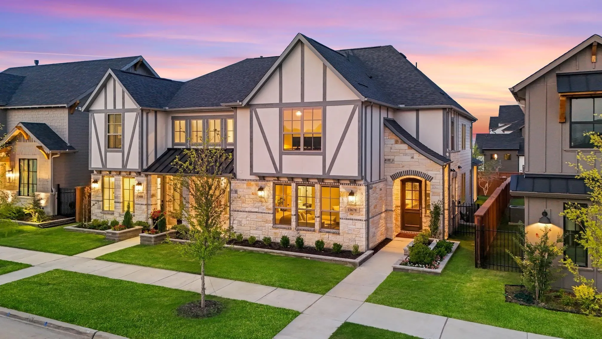 Tudor-style exterior with stone and timber accents, dark shingle roof, arched entryway, manicured lawns, and well-maintained landscaping