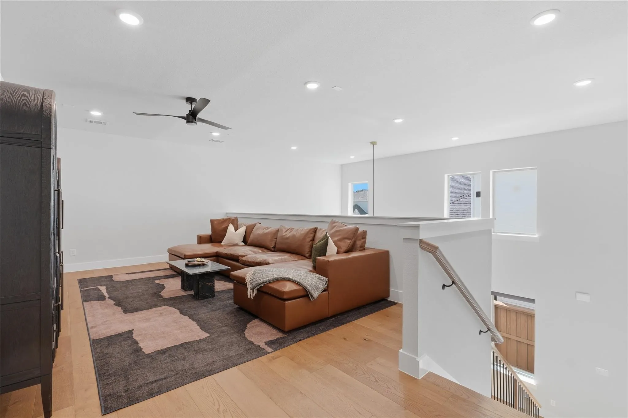 Recessed lighting, wood-finish flooring, staircase with wood handrail and metal balusters, and a ceiling fan