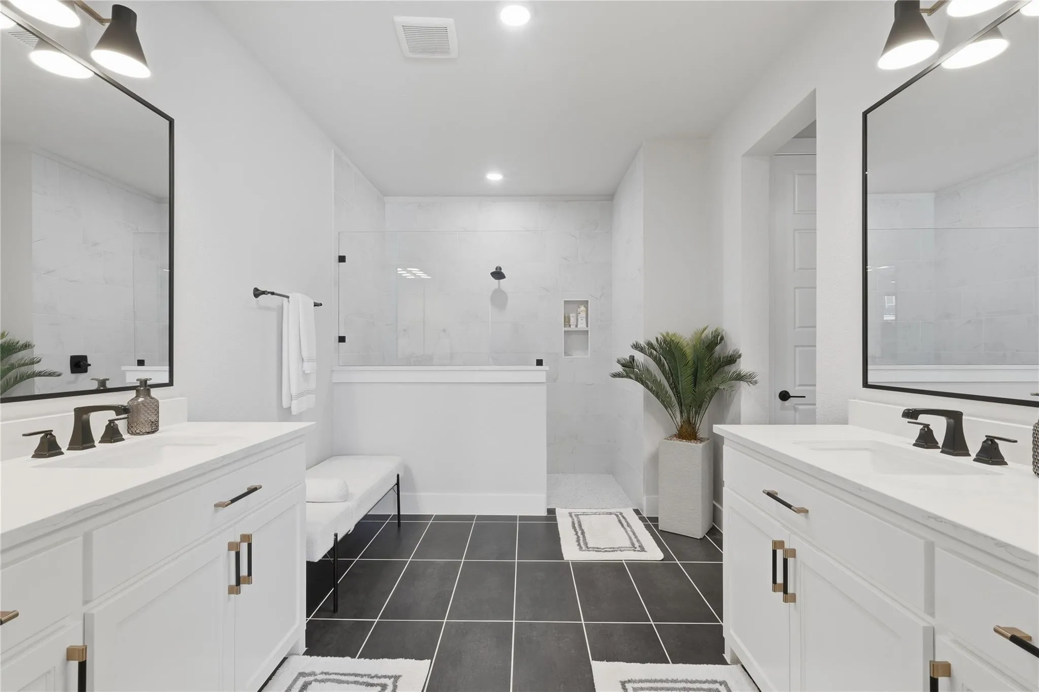 Dual white vanities with integrated sinks, black framed mirrors, walk-in shower with glass enclosure, recessed lighting, and dark tile flooring