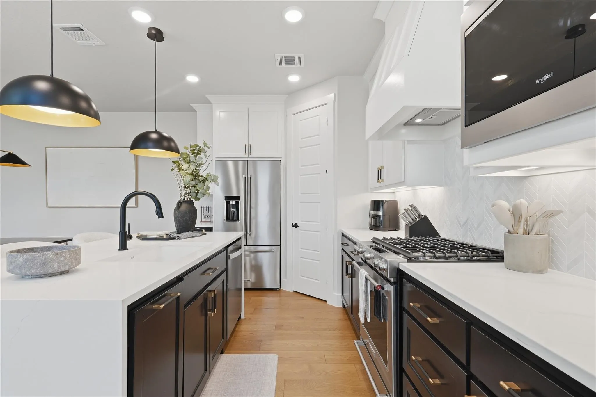 White countertops, stainless steel appliances, dark lower cabinetry, and light wood-finish flooring