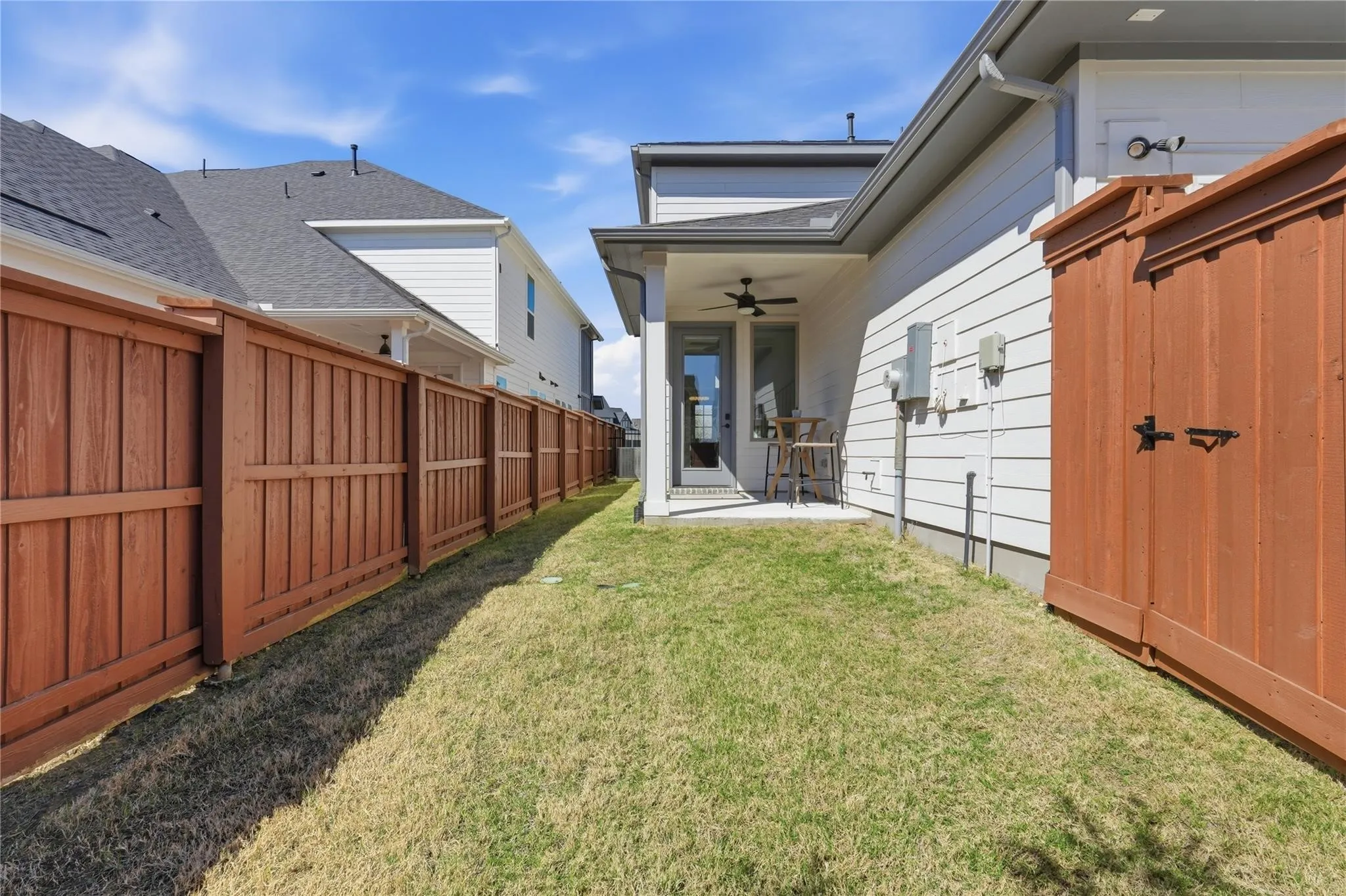 Private backyard with wooden fencing, concrete patio, and an outdoor ceiling fan