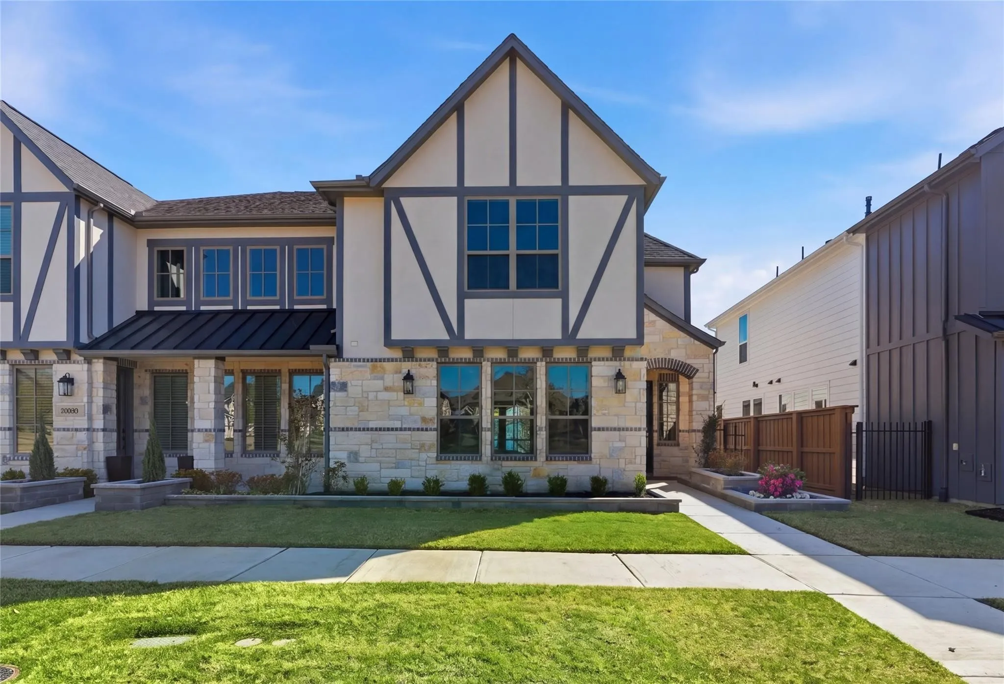 Tudor-style exterior with stone and stucco facade, featuring dark trim accents and a metal roof over the entry