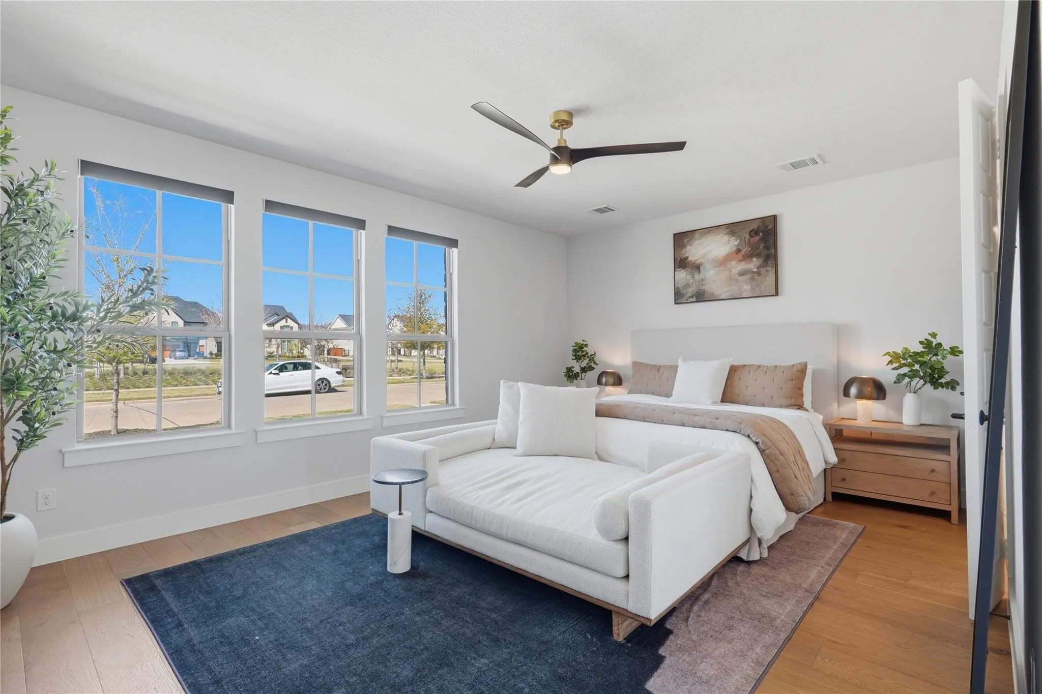 Hardwood flooring, three large windows, white walls, built-in ceiling fan with light fixture, and a built-in upholstered headboard