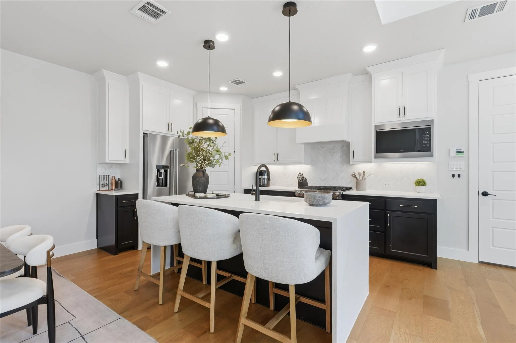 Kitchen featuring an expansive island with seating, pendant lighting, stainless steel appliances, white cabinetry, and wood-finish flooring