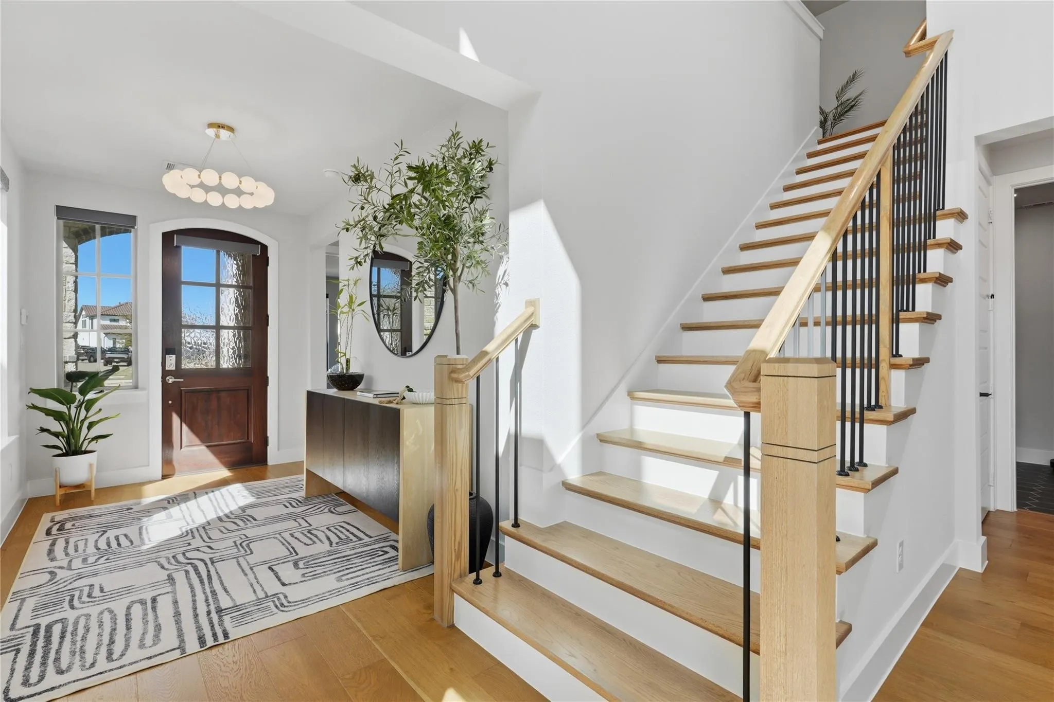 Hardwood flooring, wood staircase with black metal balusters, and a front entry door with glass panels