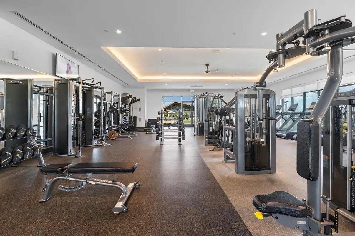 Spacious fitness area featuring extensive exercise equipment, rubber flooring, recessed lighting, and large windows