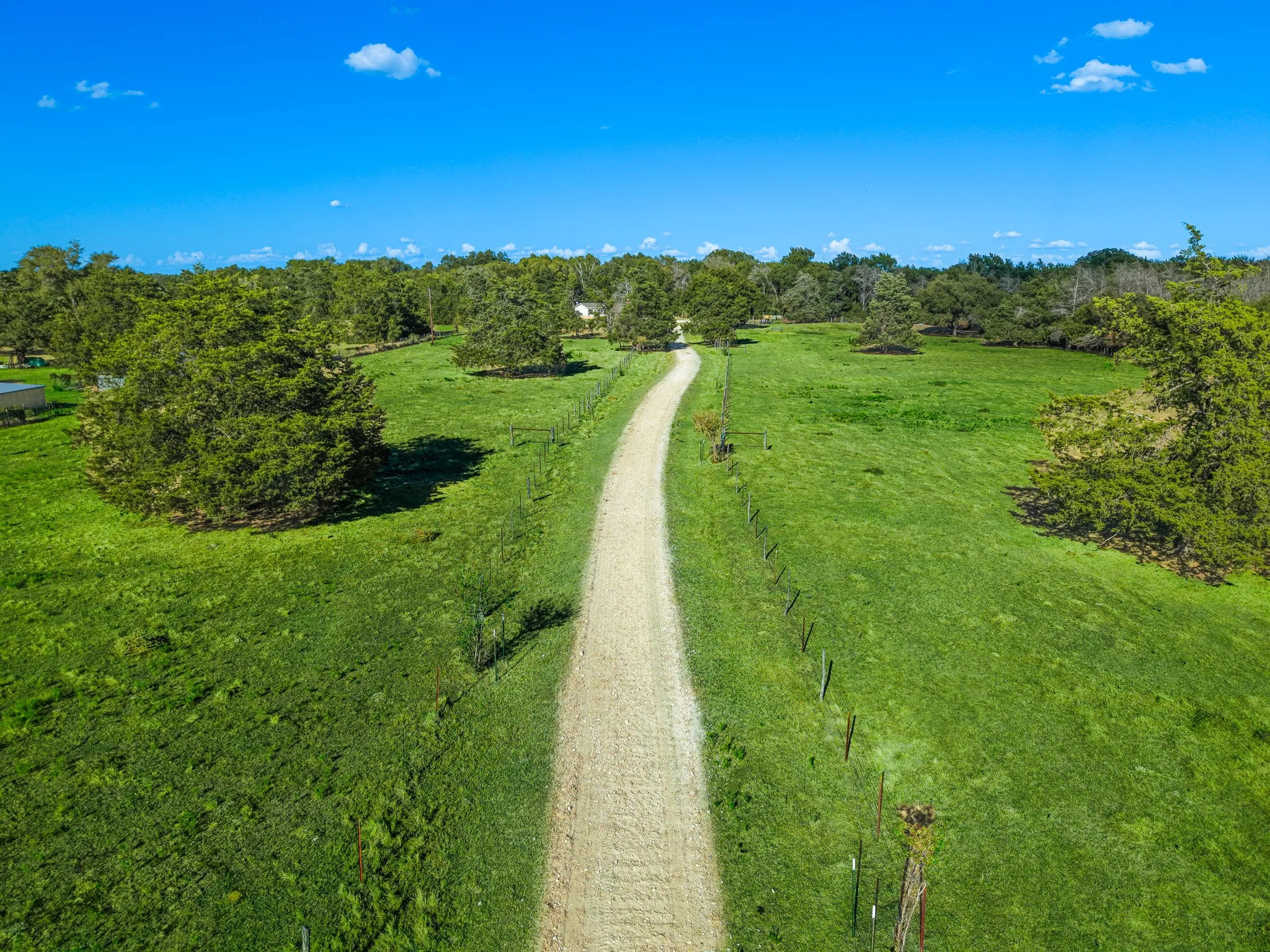 Expansive grounds featuring a meandering gravel drive, verdant lawns, mature trees, and clear blue skies