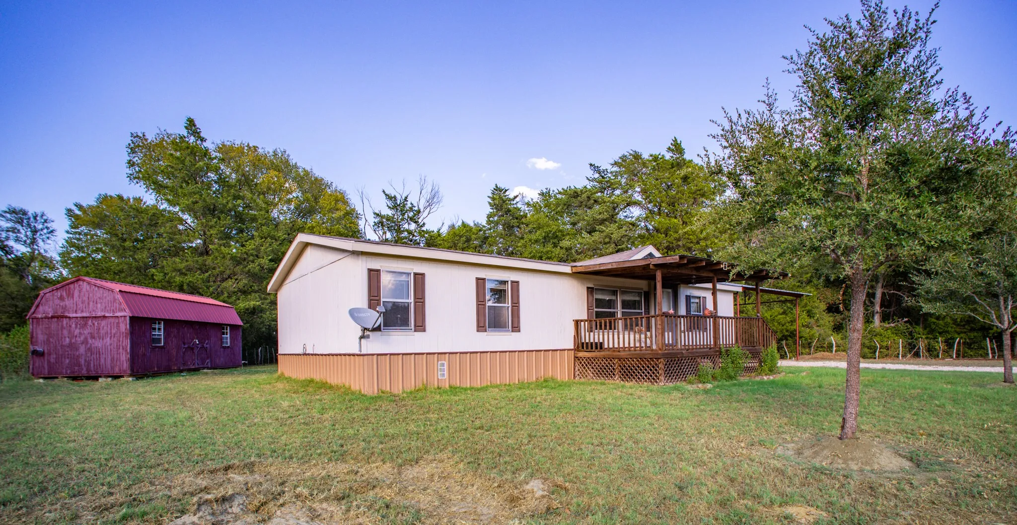 Exterior residence featuring a covered wooden deck, white siding, brown trim, and a separate red-roofed storage shed