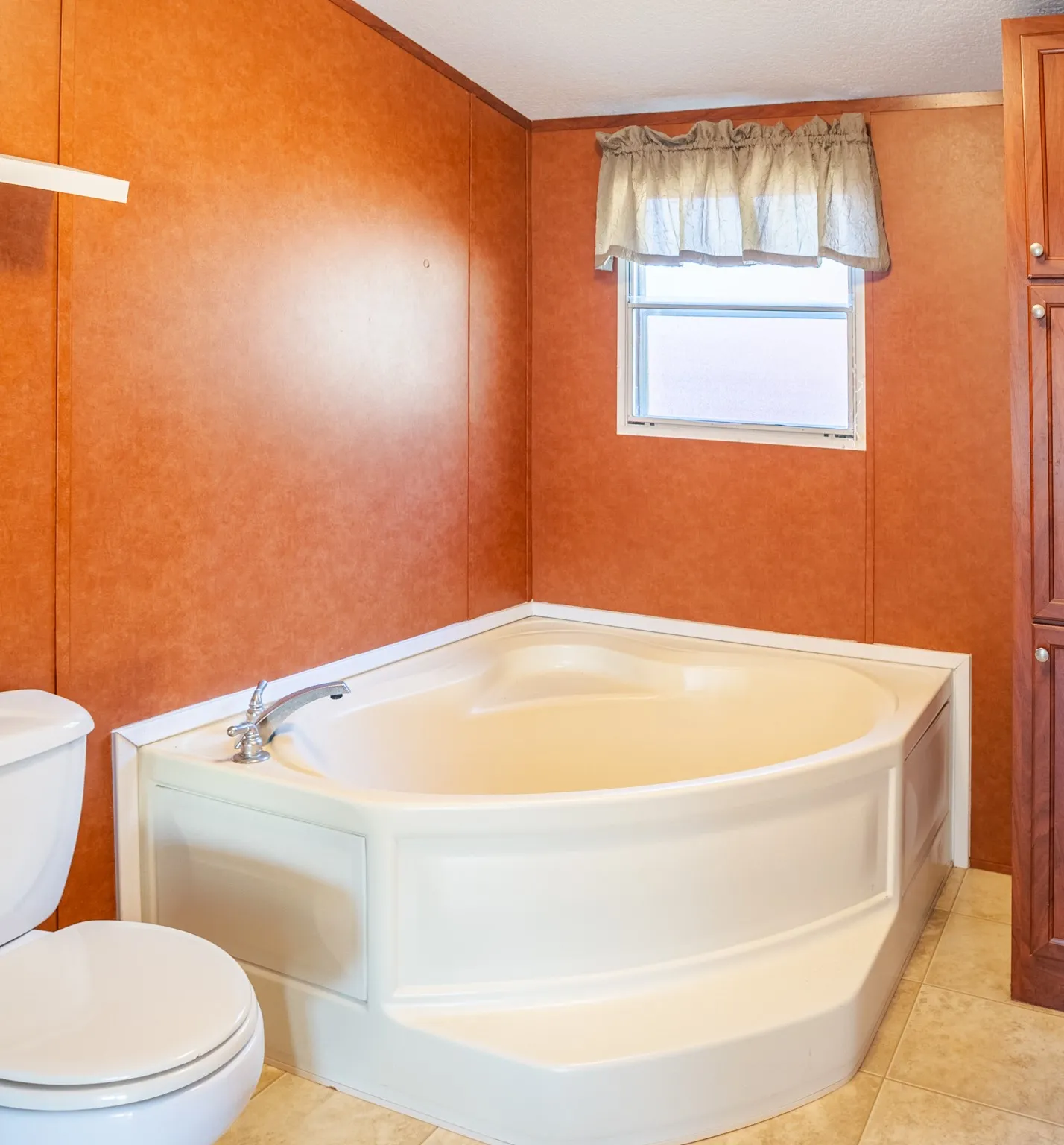 Corner soaking tub with polished chrome fixtures, paneled wall finish, and tiled flooring