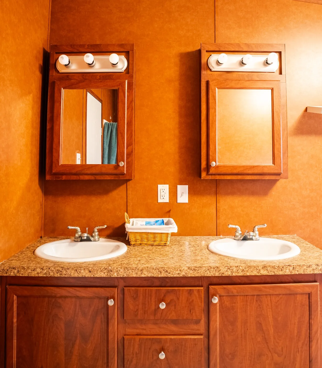 Dual vanity with integrated sinks, wood-finish cabinetry, and framed mirrors with overhead lighting