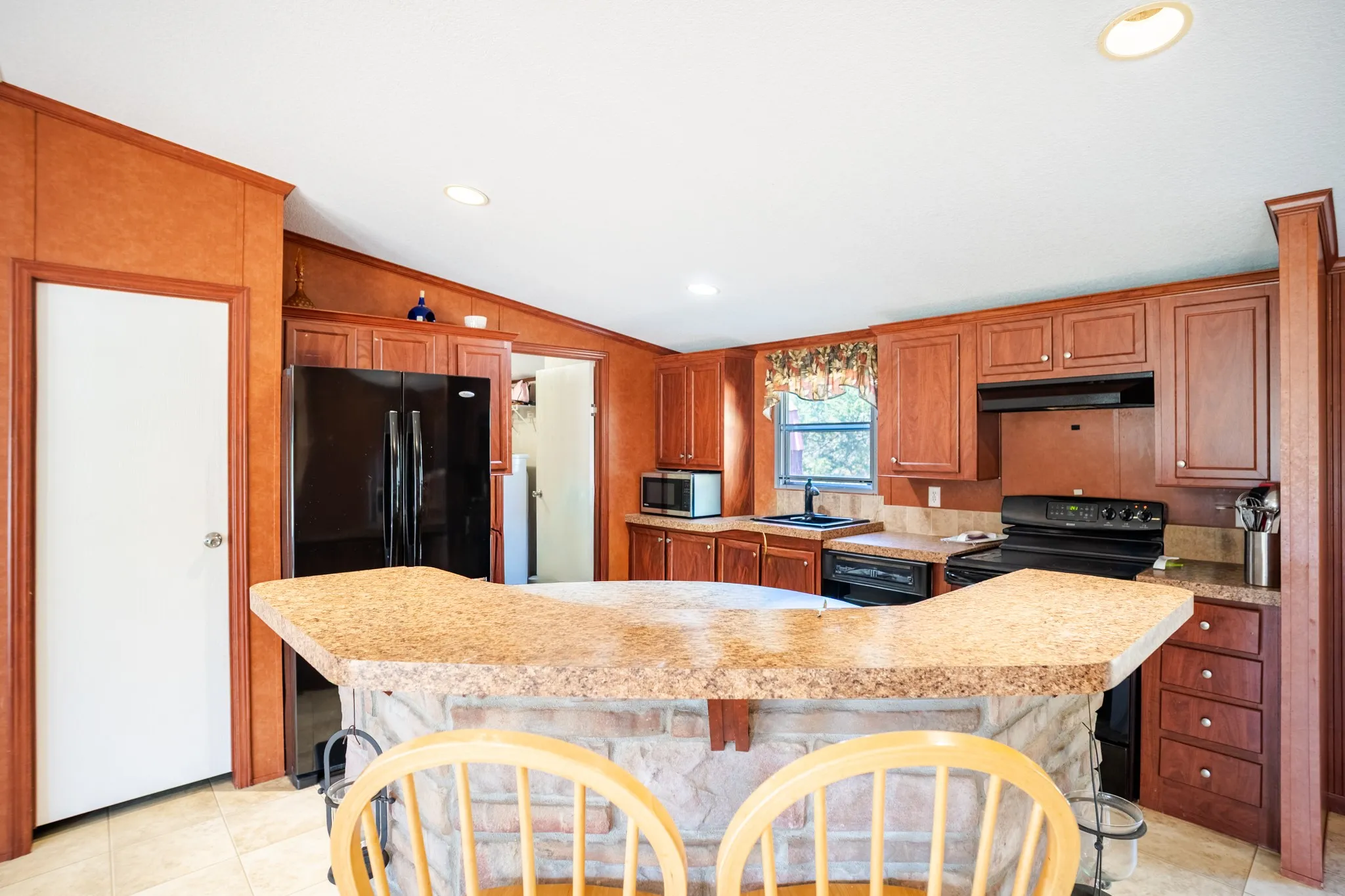 Built-in black appliances, recessed lighting, wood-finish cabinetry, stone-finish countertops, and an eat-at island with a stone-finish base