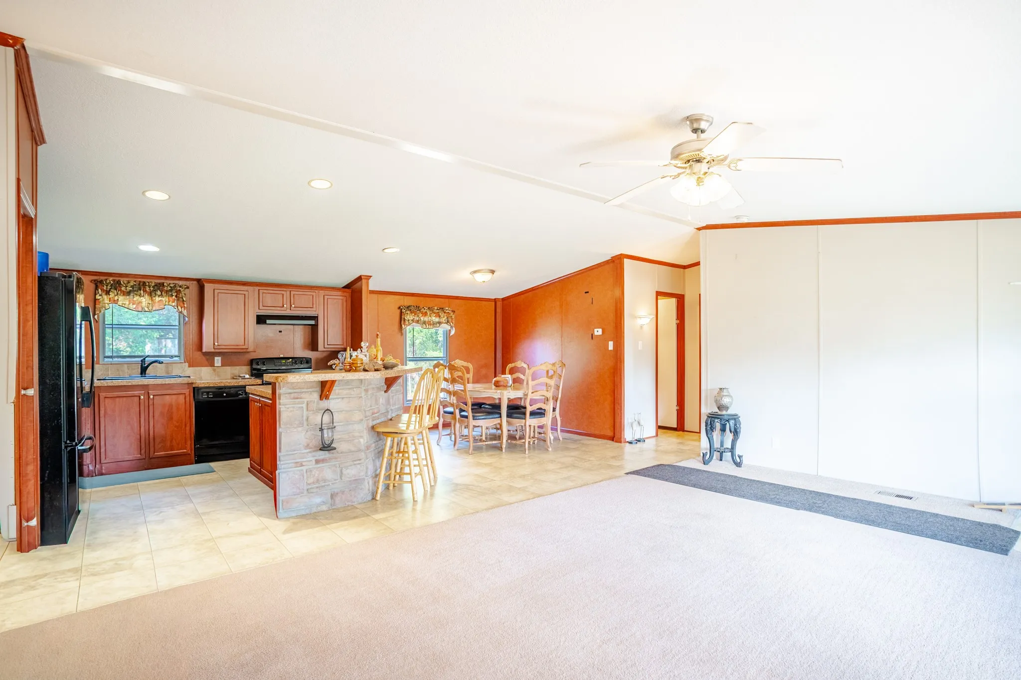 Open-concept living space featuring a kitchen with wood-finish cabinetry, black appliances, and a breakfast bar with stone-look paneling