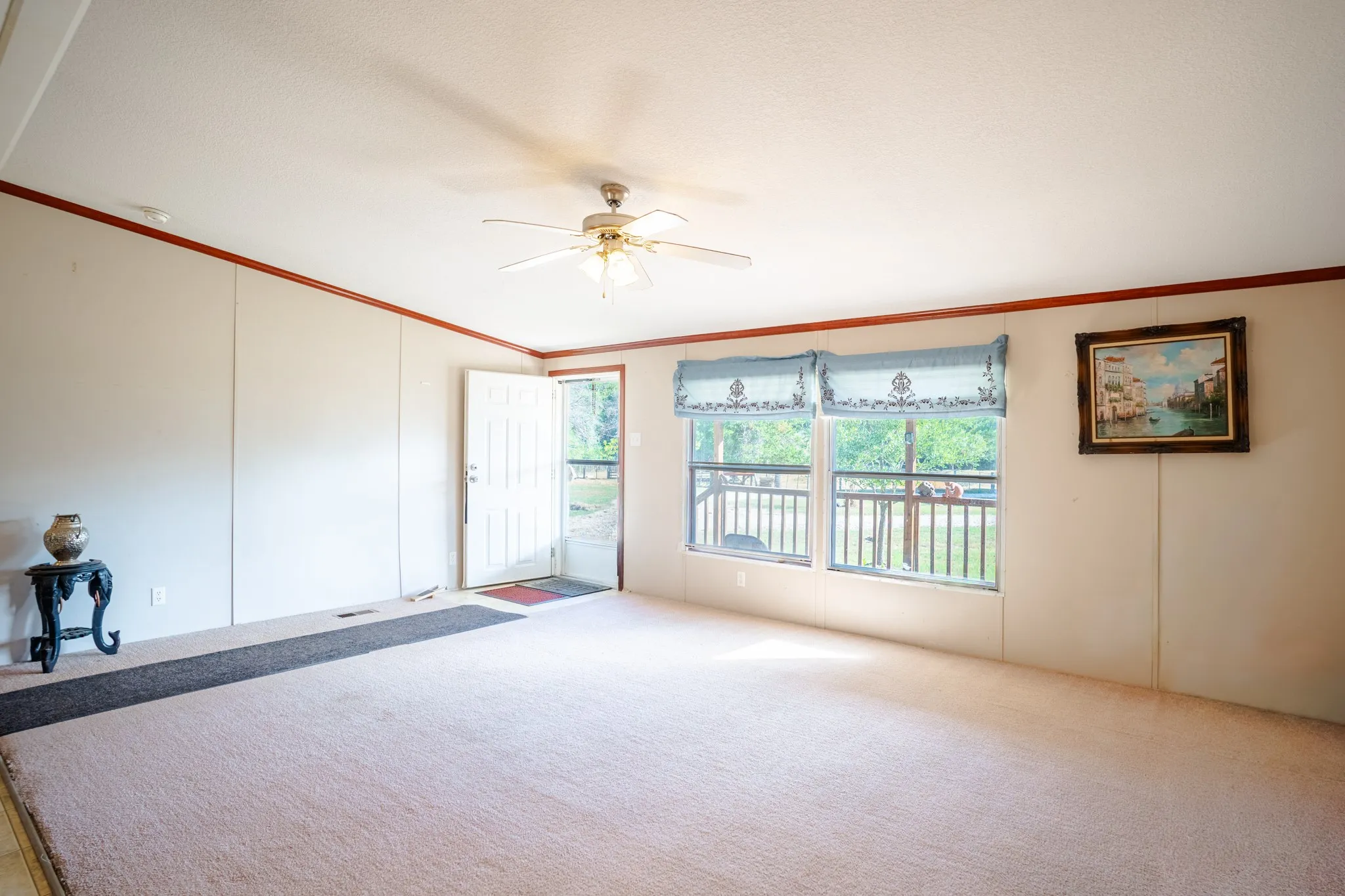 Light-colored carpeting, multiple windows, ceiling fan with light fixture, and wood trim accents