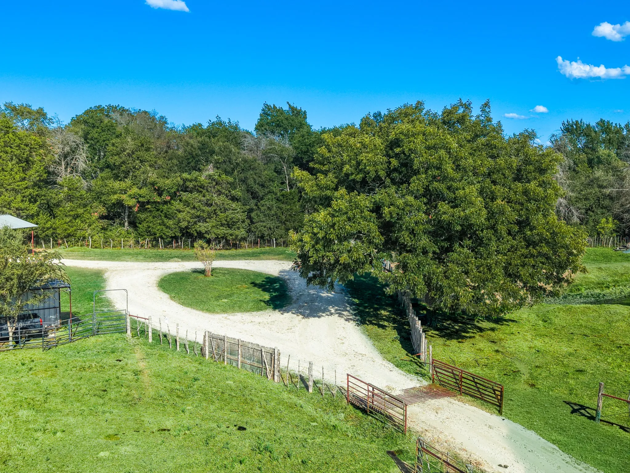 Circular gravel driveway with a central grassy island, surrounded by expansive green grounds and mature trees